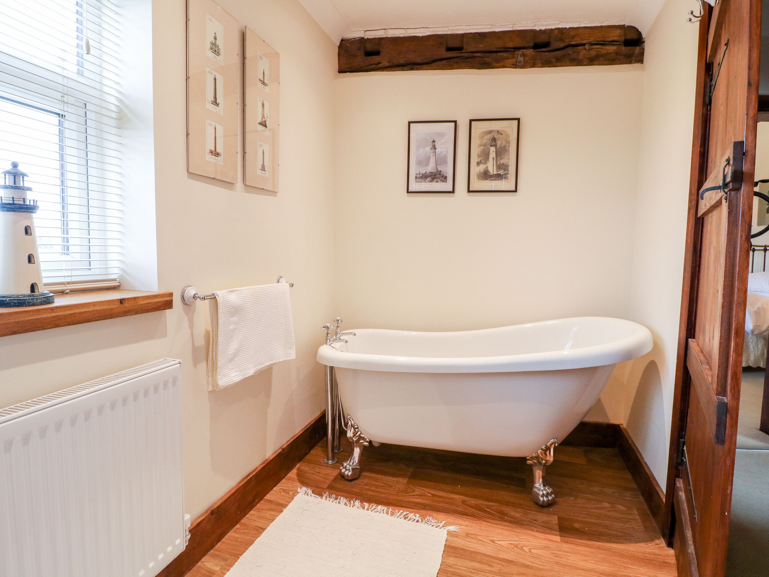 Une salle de bain avec une baignoire sur pieds, un plancher en bois, un radiateur blanc et une fenêtre avec des stores.