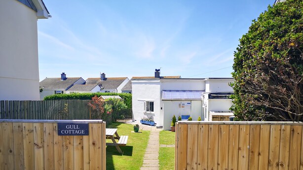 A gated entrance to a cottage named 'Gull Cottage' with a paved pathway leading to a grassy area and a small garden. - Gull Cottage (Tintagel)