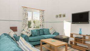 A modern living room with a teal sofa, a wooden coffee table, and a flat-screen TV mounted on the wall. - Gull Cottage (Tintagel)