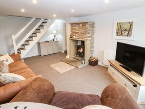 A living room with a stone fireplace, a television, a sofa, and a staircase. - Wren Cottage (Oldham)