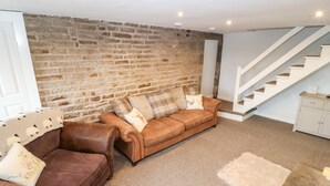 Una sala de estar con una pared de ladrillo, un sofá de cuero marrón, una puerta blanca y una escalera.