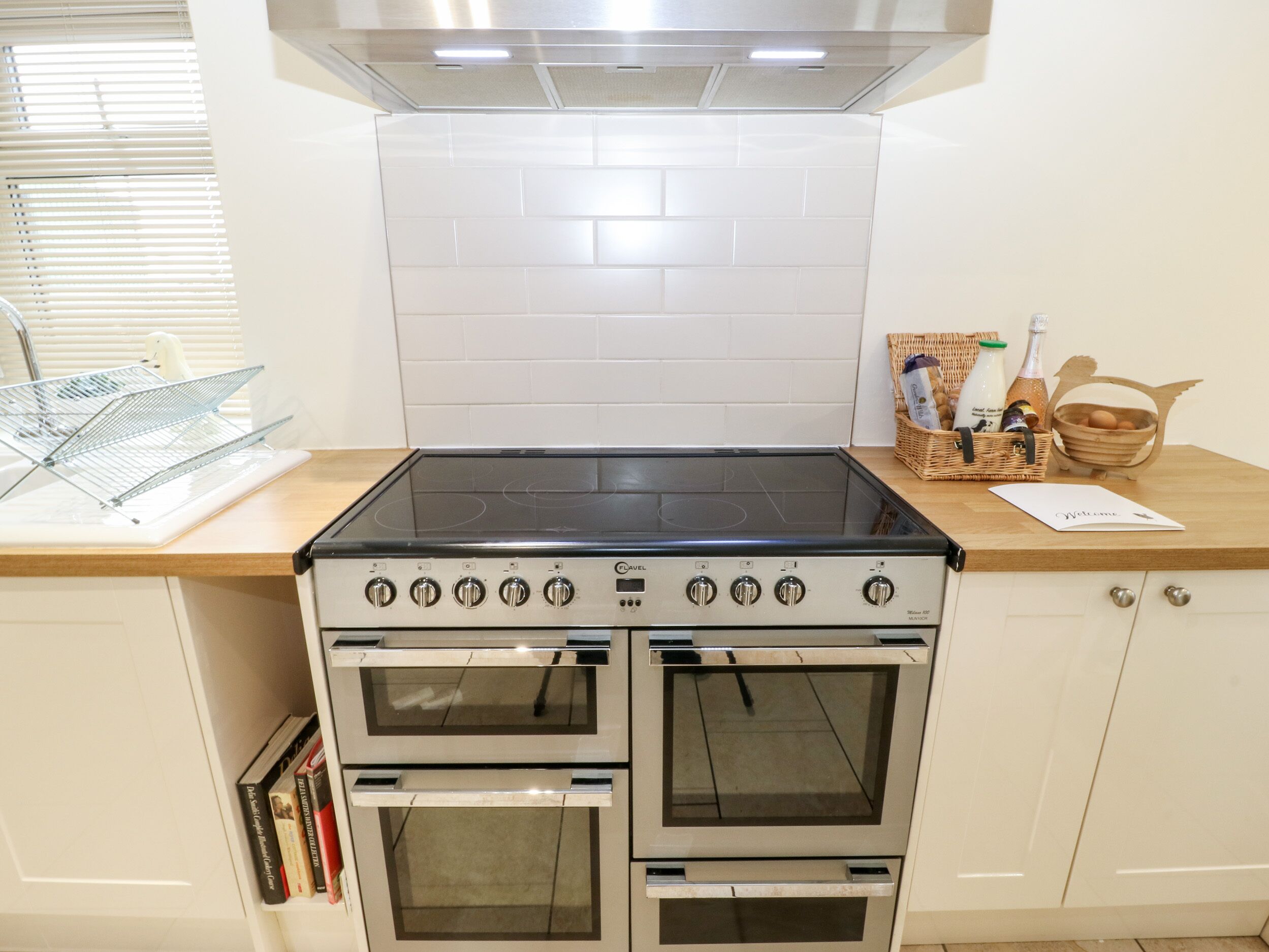 Een keuken met een gasfornuis, twee ovens, een roestvrijstalen afzuigkap en een houten aanrechtblad.