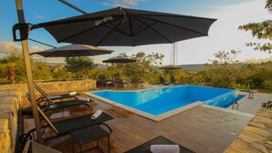 Piscina exterior con sillones de descanso y sombrillas, rodeada de muros de piedra y vegetación.