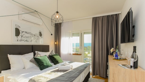 Un dormitorio moderno con cama, escritorio, televisor y ventana con cortinas.