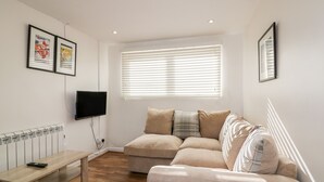 A modern living room with a beige sofa, a wooden bench, and a flat-screen TV mounted on the wall. - Cove Cottage (Tintagel)