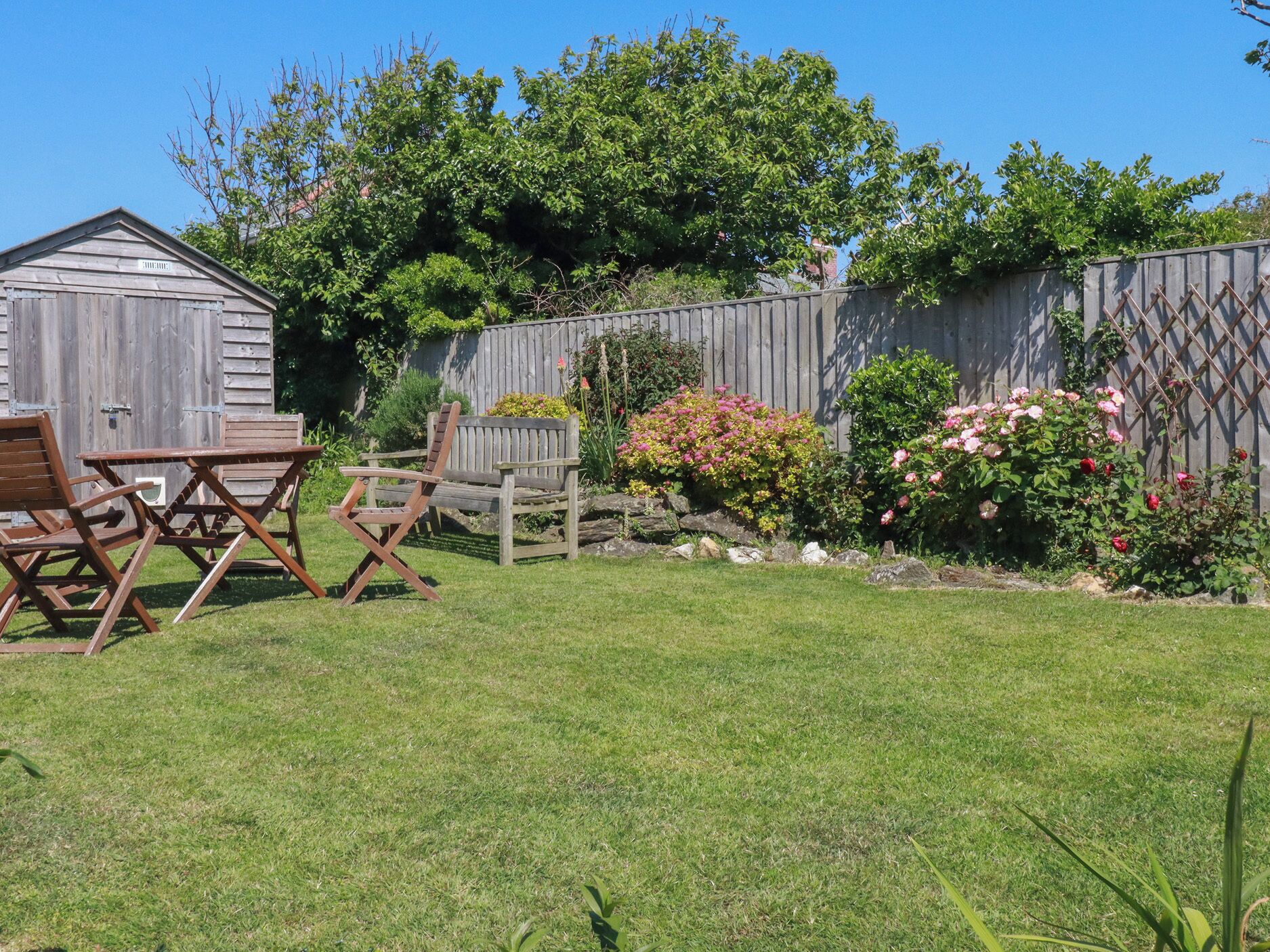 Ein Garten mit einem Holzschuppen, einem Holzzaun und verschiedenen Pflanzen und Blumen.