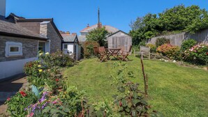 A garden with a wooden table and chairs, a shed, and a stone building. - Cove Cottage (Tintagel)