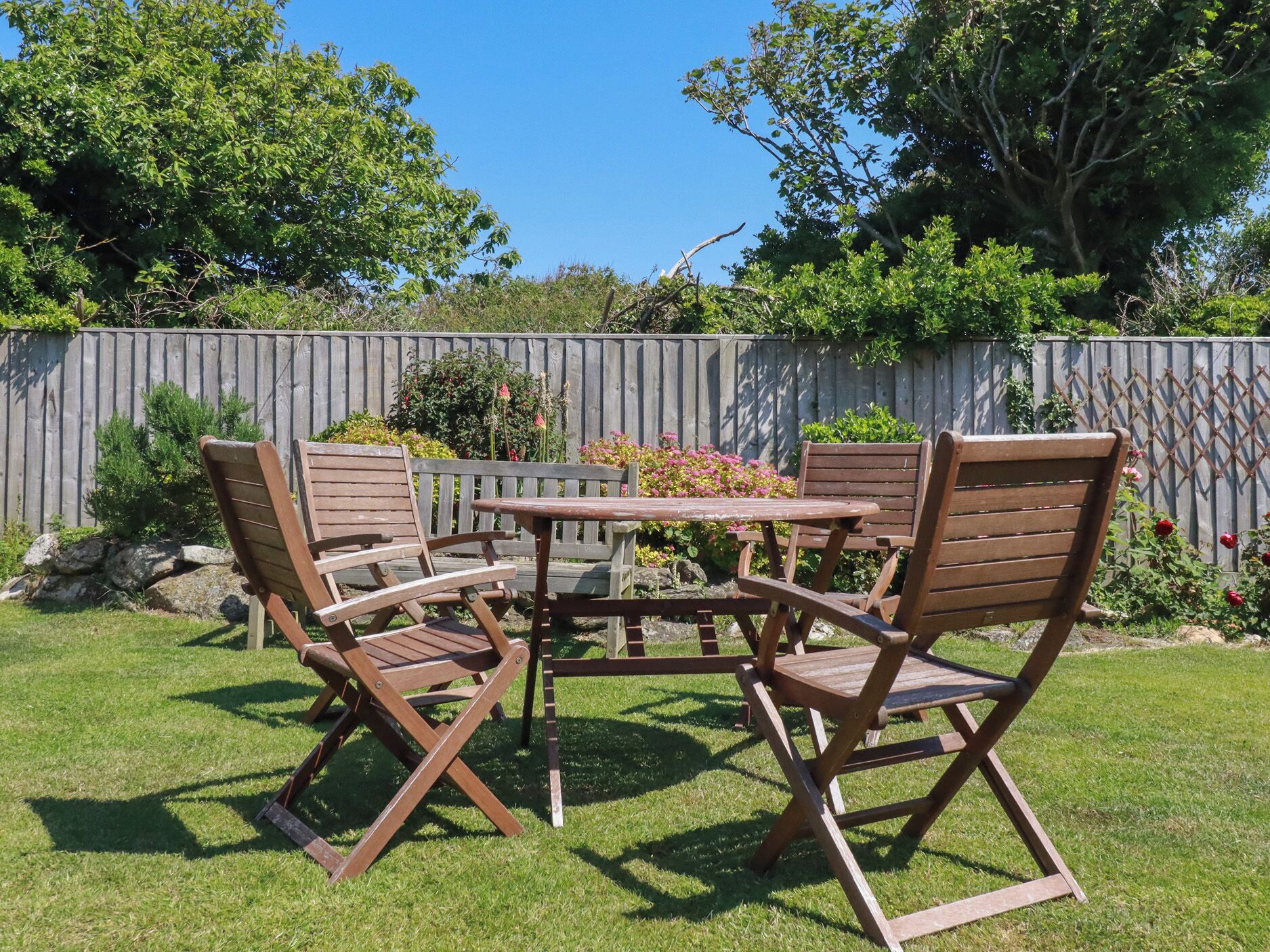 Een terras met een houten tafel en stoelen, omgeven door een houten hek en begroeiing.