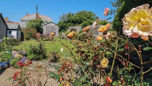 A garden with a variety of flowers, a wooden shed, and a stone wall. - Cove Cottage (Tintagel)