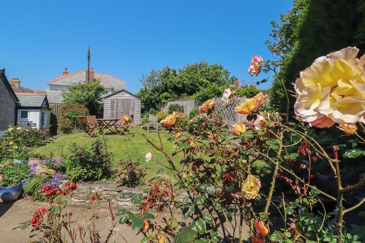 A garden with a variety of flowers, a wooden shed, and a stone wall.