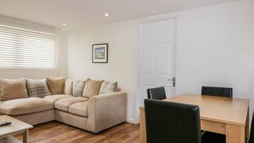 A modern living room with a beige sectional sofa, a wooden dining table, and black chairs.