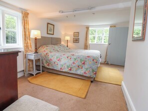 A bedroom with a bed, bedside tables, a dresser, two windows with curtains, and a door. - Wolvesacre Mill Cottage (Whitchurch)