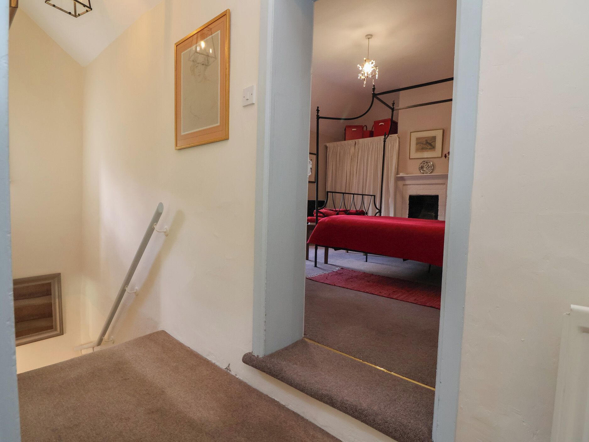 Una escalera conduce a un dormitorio con cama, chimenea y candelabro.