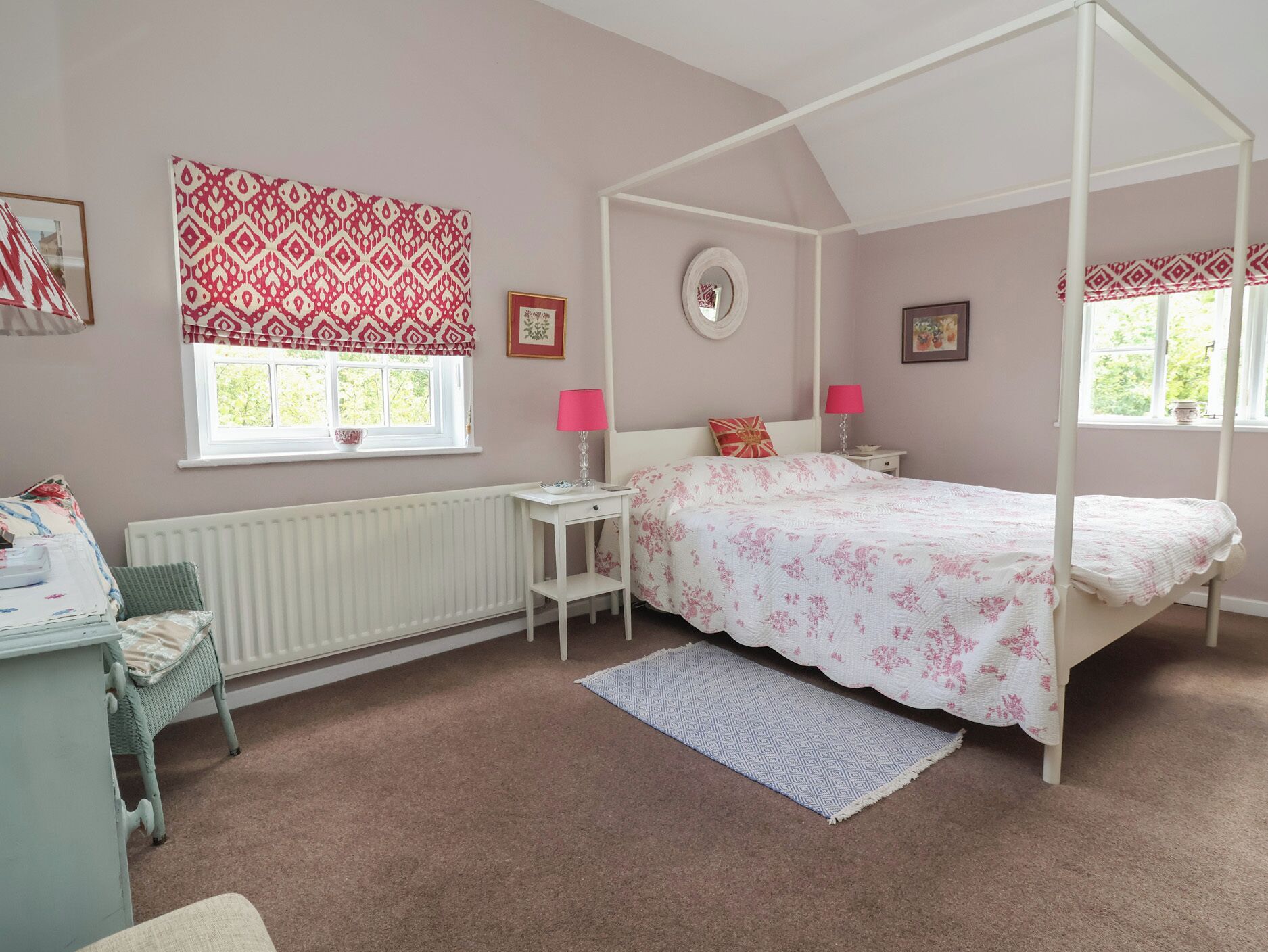A bedroom with a four-poster bed, a window with a view, a radiator, a bedside table, and a chair.