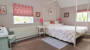 A bedroom with a four-poster bed, a window with a view, a radiator, a bedside table, and a chair.
