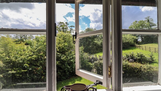 Una ventana que da a un paisaje verde, una valla de madera y un objeto metálico en el alféizar.