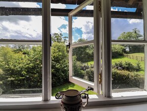 A window with a view of a green landscape, a wooden fence, and a metal object on the windowsill. - Wolvesacre Mill Cottage (Whitchurch)