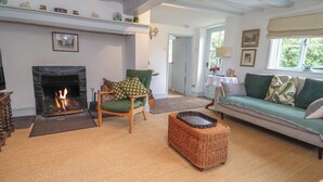 Una sala de estar acogedora con chimenea, un sillón verde, un reposapiés de mimbre y un sofá con cojines estampados.