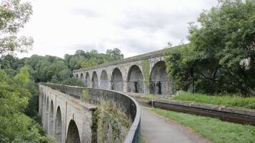 A stone viaduct with multiple arches, surrounded by lush greenery and a paved path.