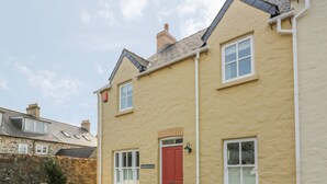 A two-story building with a red door, white windows, and a stone wall in the background.