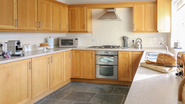 A modern kitchen with wooden cabinets, a microwave, an oven, and a bread loaf on the counter.