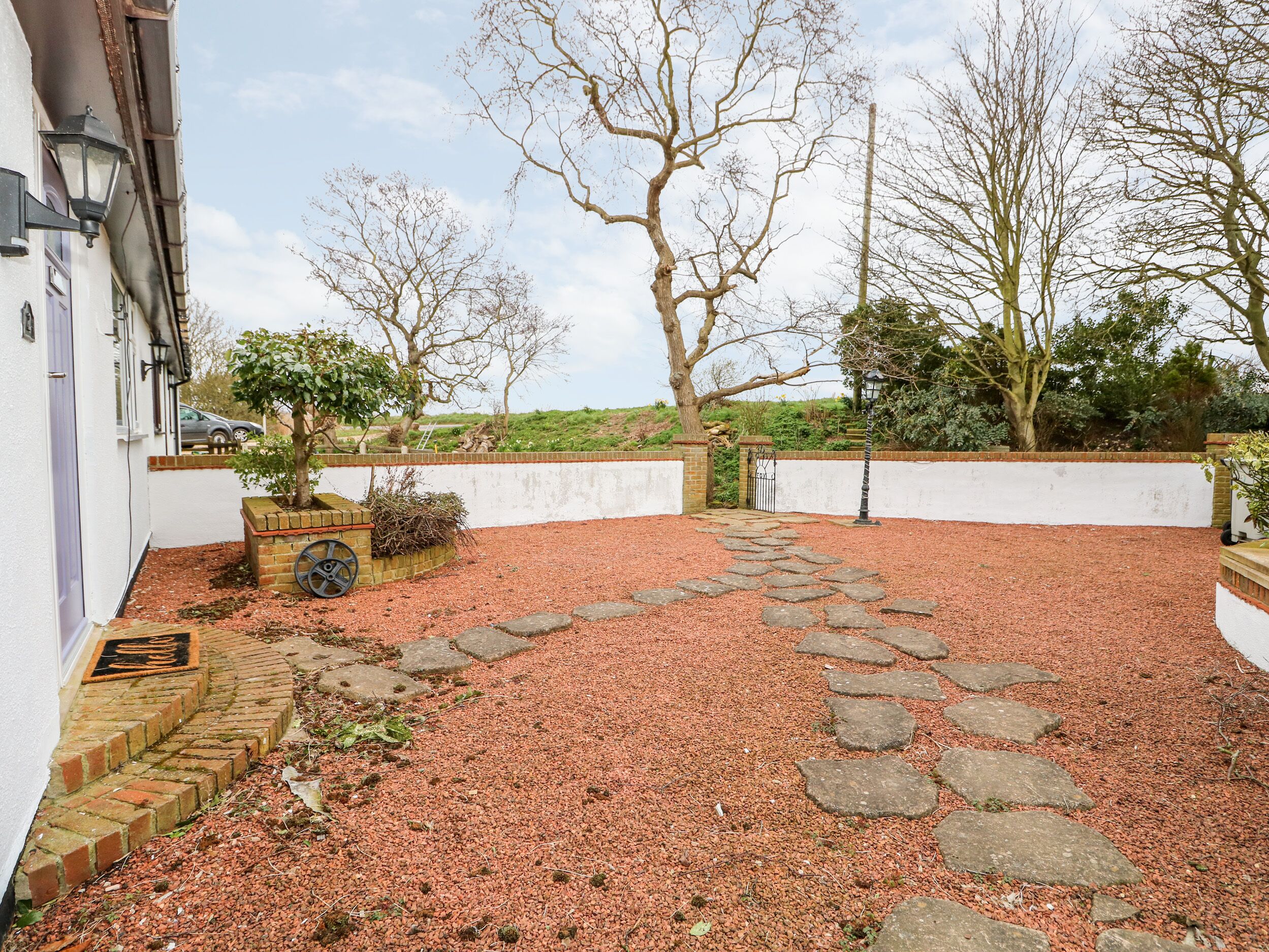 Un patio con camino de grava, una jardinera de ladrillo y un árbol.