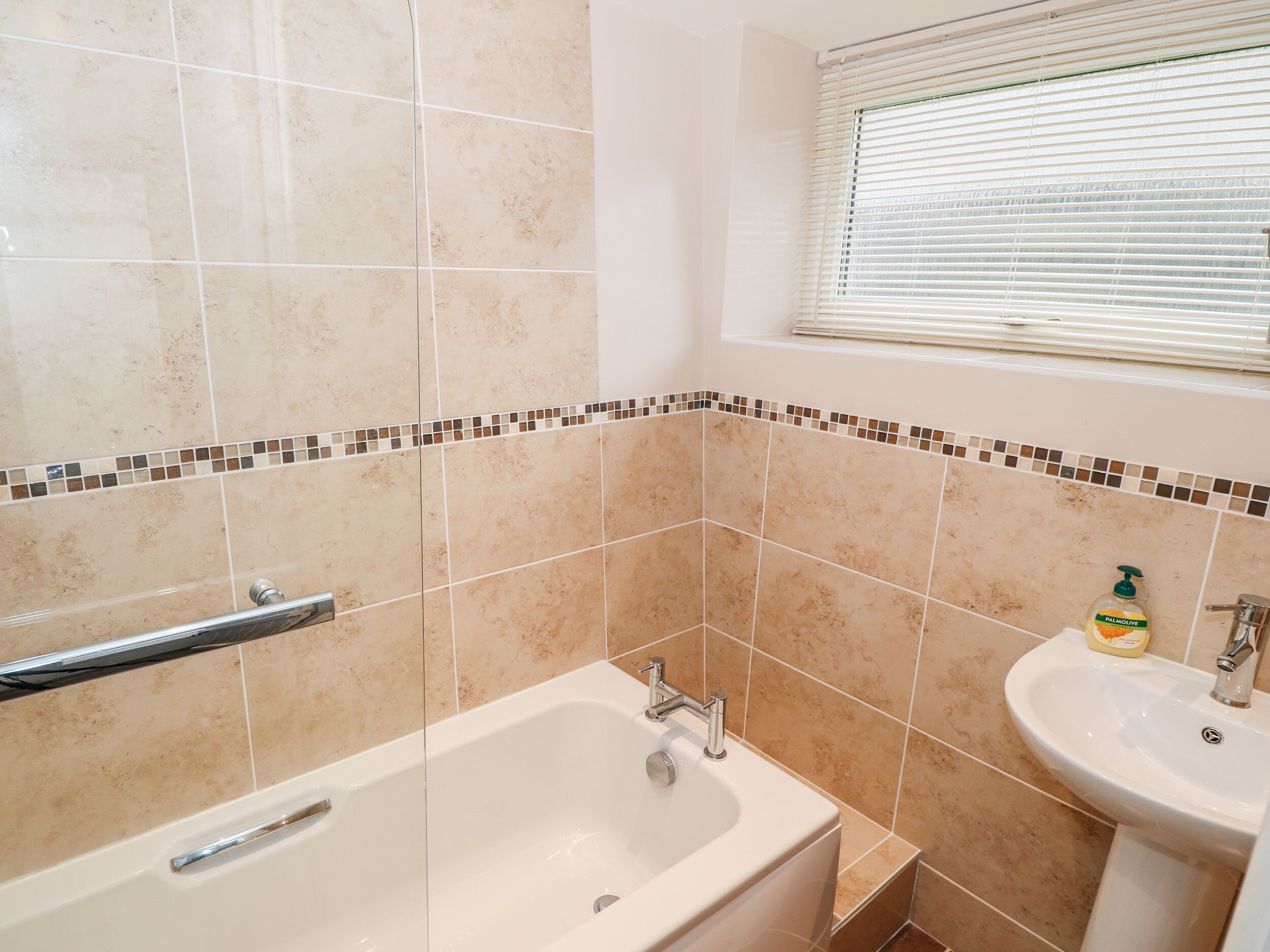 A bathroom with a bathtub, a sink, and a window with blinds.