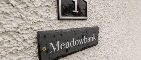 A house number '1' and a nameplate 'Meadowbank' mounted on a textured wall.