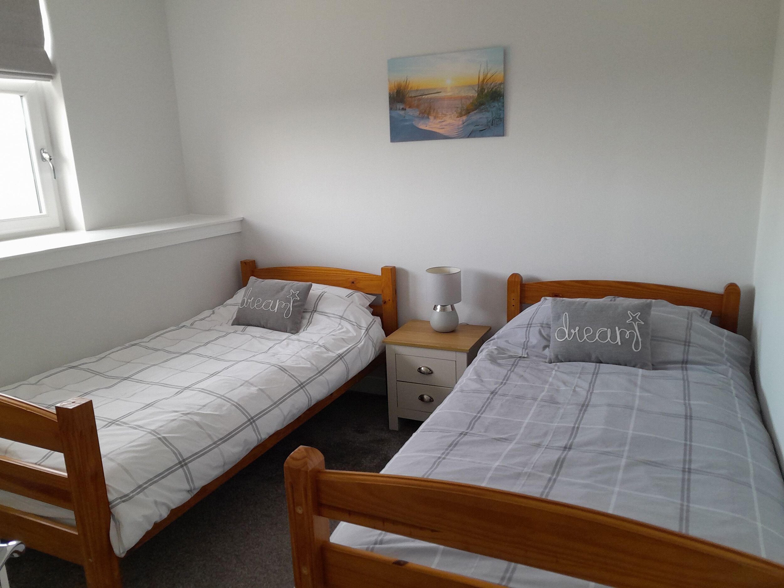 Une chambre avec deux lits simples, une table de chevet, une lampe et un tableau au mur.