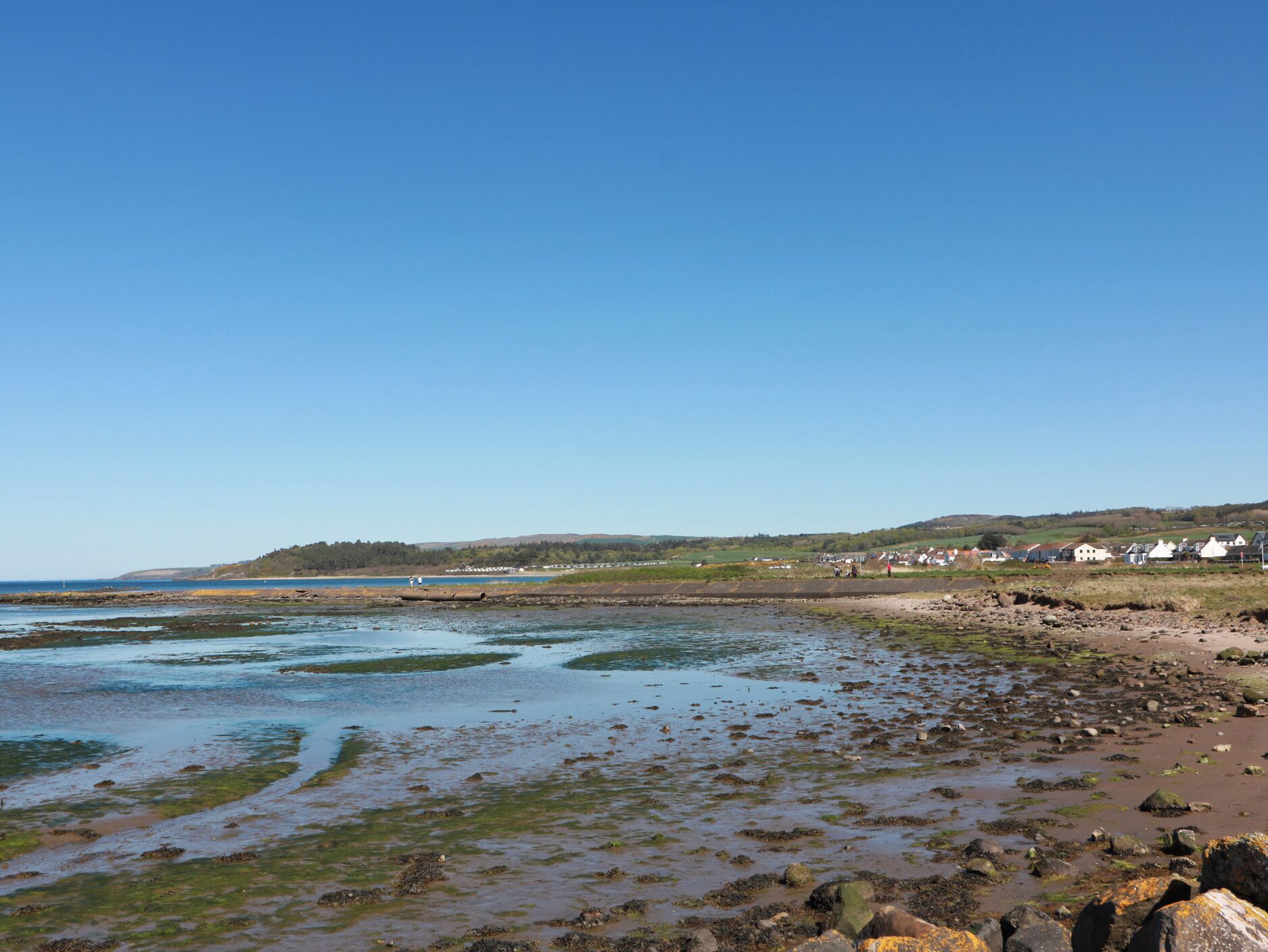 Eine Küstenlandschaft mit Strand, felsigem Ufer und Häusern im Hintergrund.
