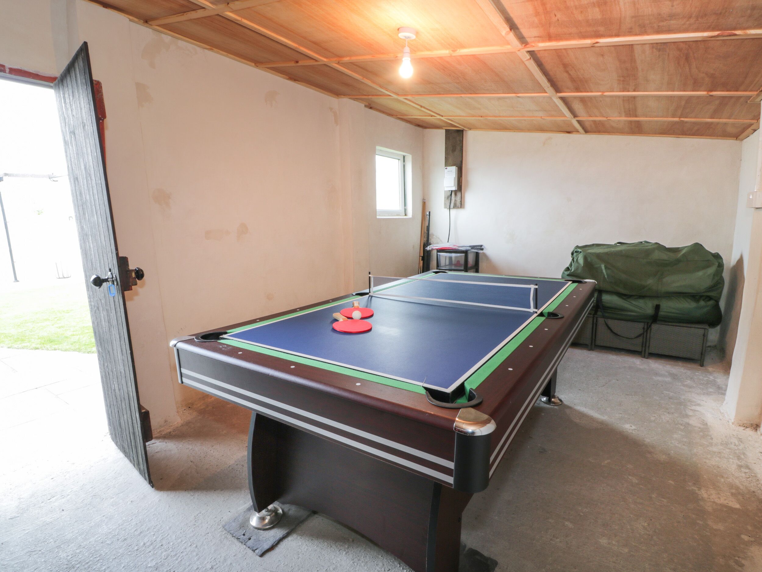 Una mesa de ping pong en una habitación con techo de madera y una puerta que da al exterior.