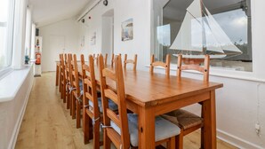 A dining area with a wooden table and chairs, a large window with a sailboat model, and a white wall with a fire extinguisher and a framed picture. - Trevena Lodge (Tintagel)