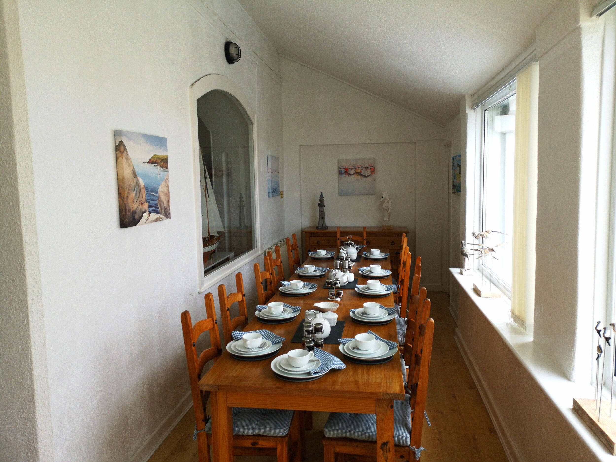 Ein Esszimmer mit einem langen Holztisch, der für eine Mahlzeit gedeckt ist und von Stühlen gesäumt wird.