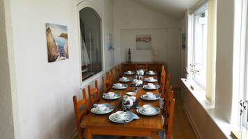 Ein Esszimmer mit einem langen Holztisch, der für eine Mahlzeit gedeckt ist und von Stühlen gesäumt wird.