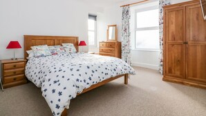 A bedroom with a wooden bed, two bedside tables, a dresser, a mirror, and a wardrobe. - Trevena Lodge (Tintagel)