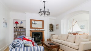A living room with a fireplace, a bookshelf, a striped armchair, a beige sofa, and a wooden coffee table. - Trevena Lodge (Tintagel)