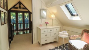 Ein Schlafzimmer mit schrägem Dach, einem Schminktisch, einem Stuhl, einem Spiegel und einem Fenster.
