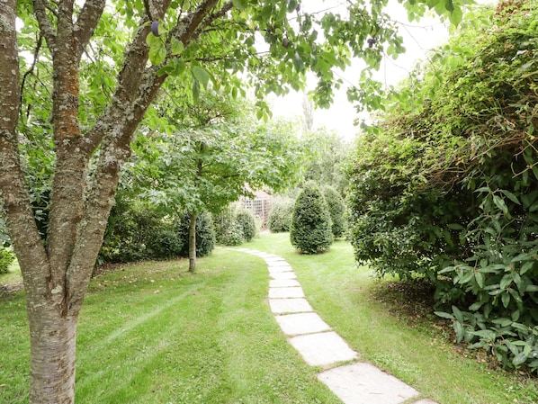 A stone pathway leading through a well-maintained garden with various shrubs and trees.