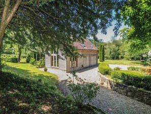 A rustic wooden building with a sloped roof, surrounded by lush greenery and a gravel path leading to it. - The Barn at Frog Pond Farm (Salisbury)