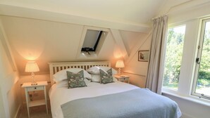 Ein Schlafzimmer mit einem Bett, zwei Nachttischen, einem Fenster mit Vorhängen, einem Oberlicht und einem kleinen Bild an der Wand.