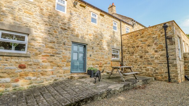 A stone building with a blue door, a small garden area, and a wooden bench.