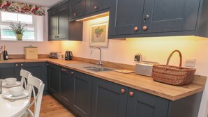 A modern kitchen with dark cabinets, a wooden countertop, and a dining area with white chairs and a table.