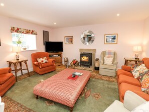 A cozy living room with a fireplace, two armchairs, a sofa, a television, and a patterned rug. - Todridge Barn (Newcastle-upon-Tyne)