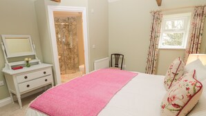 A bedroom with a bed, a dresser, a mirror, a shower, and a window with curtains.