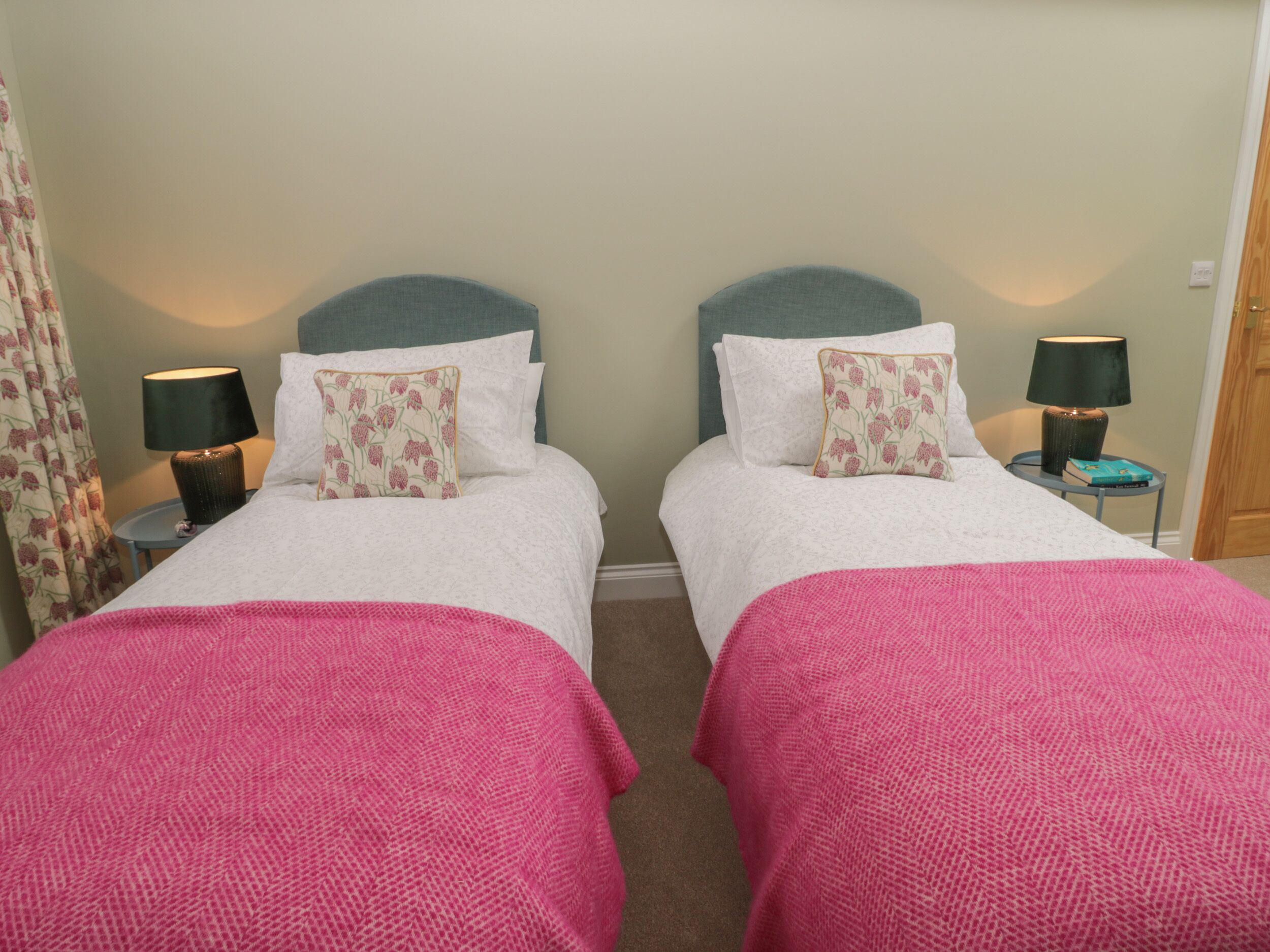 A twin room with two beds, each with a headboard, a bedside table with a lamp, and a pink blanket.