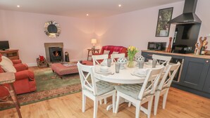 A dining area with a round table and chairs, a fireplace, a television, and a kitchen area with cabinets and a stove.