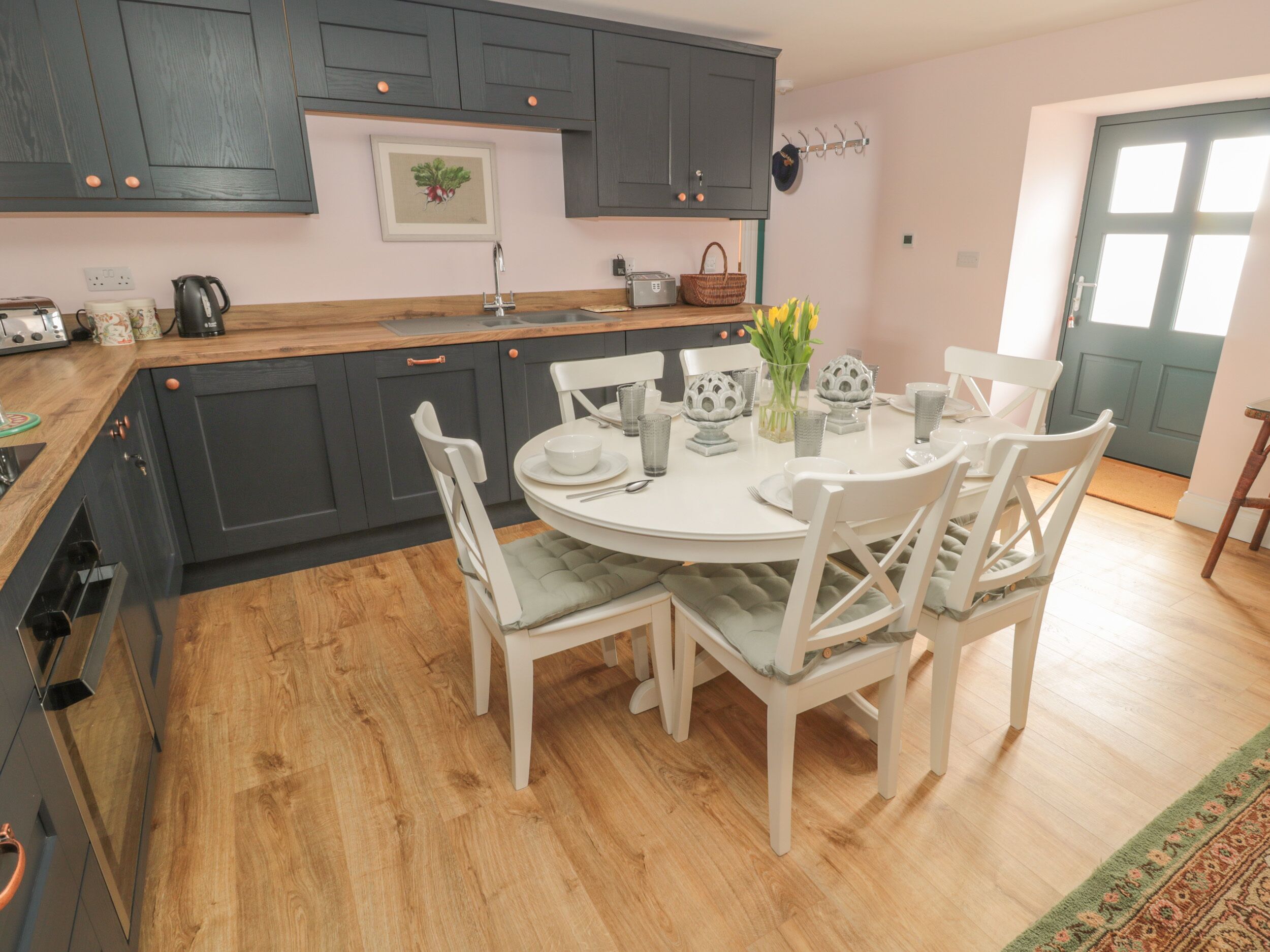 A kitchen with a round dining table, white chairs, grey cabinets, and a wooden countertop.