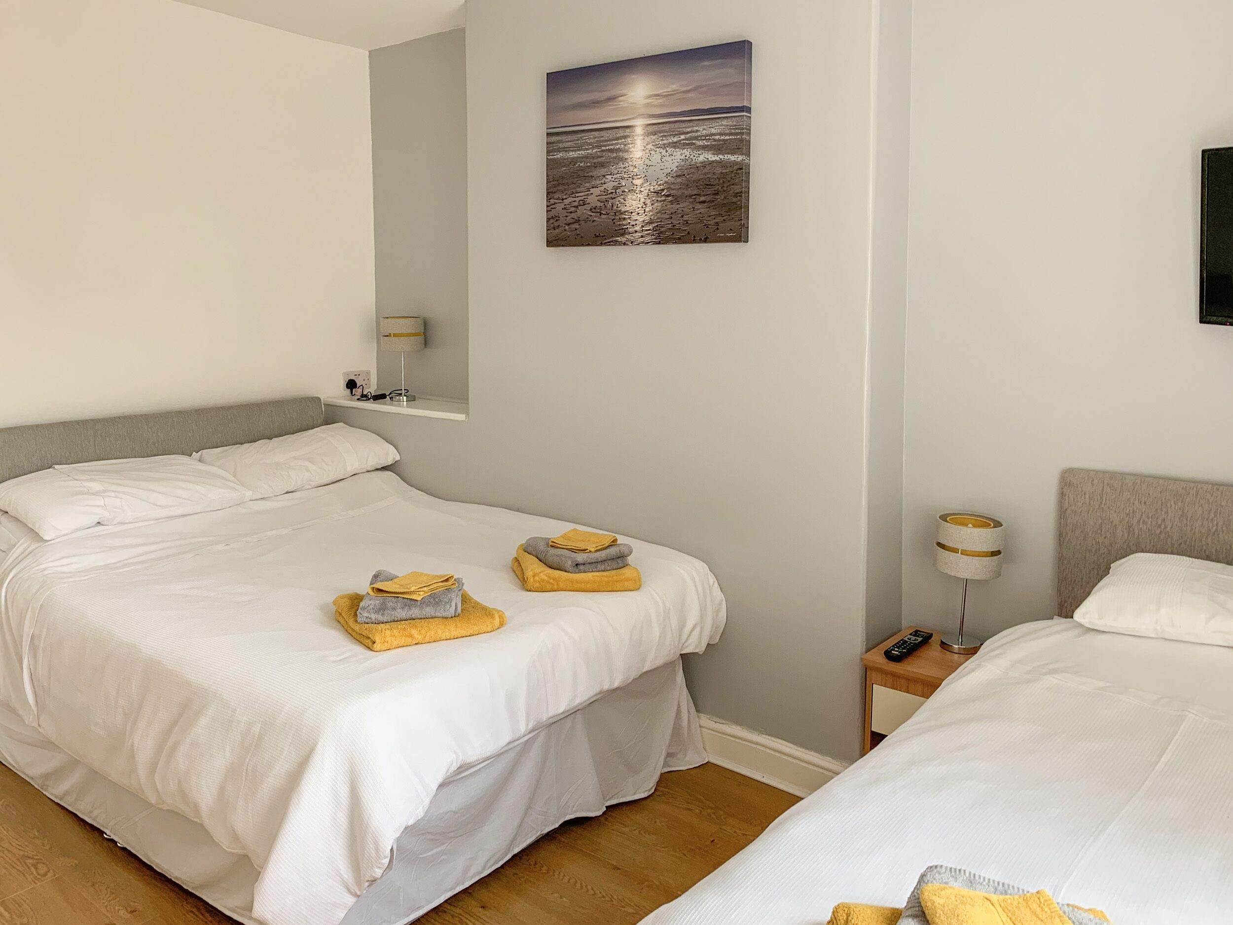 A hotel room with two beds, a nightstand, a lamp, and a painting of a sunset over the ocean.