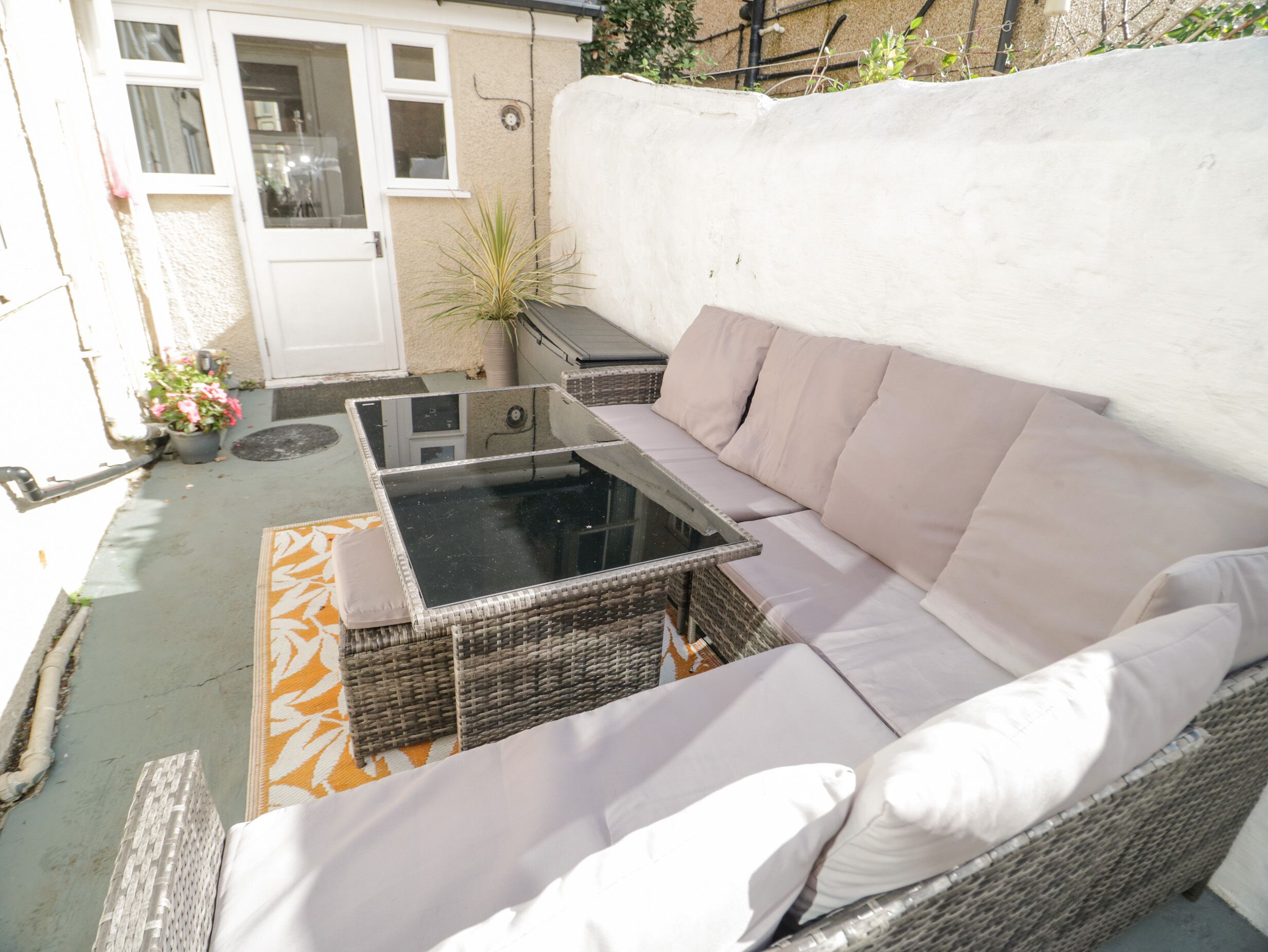 Una zona patio con un divano in vimini, un tavolo con piano in vetro e un tappeto decorato.