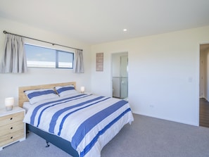 A bedroom with a bed, bedside tables, a window with curtains, a door leading to a bathroom, and a carpeted floor.
